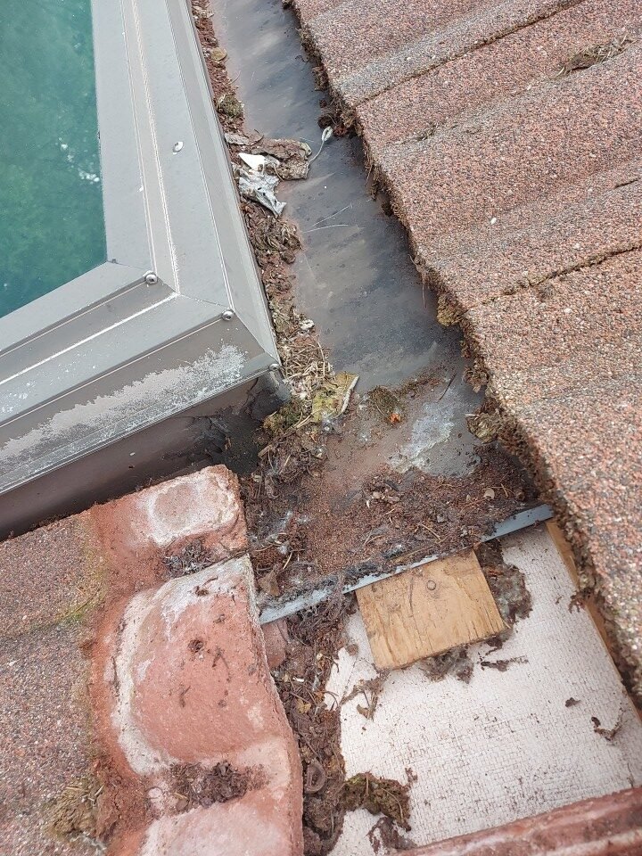 Clearing debris from the pan flashing containment lip beside the skylight on a Port Moody roof.