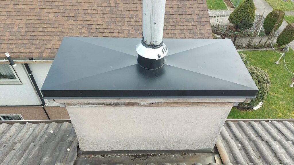 New black metal chimney chase cap installed on a stucco chimney chase in Burnaby.