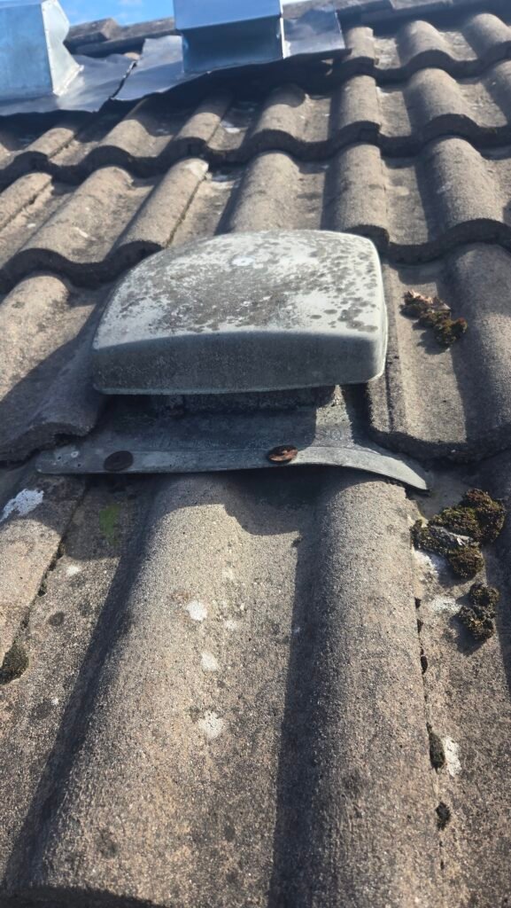 Plastic roof vent on S-shaped concrete tiles in Vancouver, its flange bent downward to follow the tile.