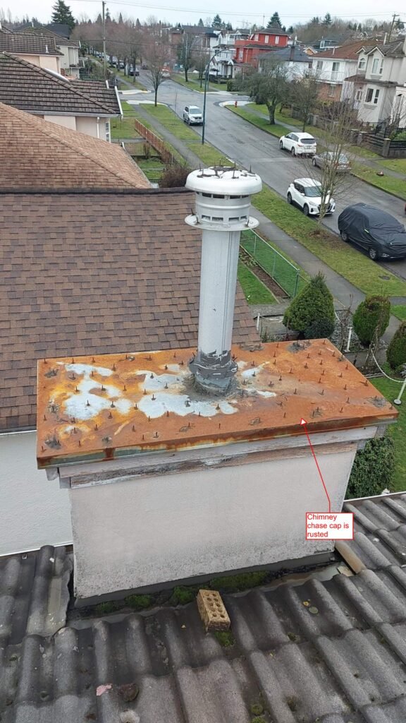 Rusted chimney chase cap covered in glued-on roofing nails to deter birds, on a Burnaby home.
