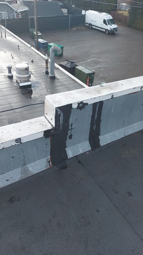 Torch-on roof flashing patched with black roof mastic on a parapet wall in Aldergrove.