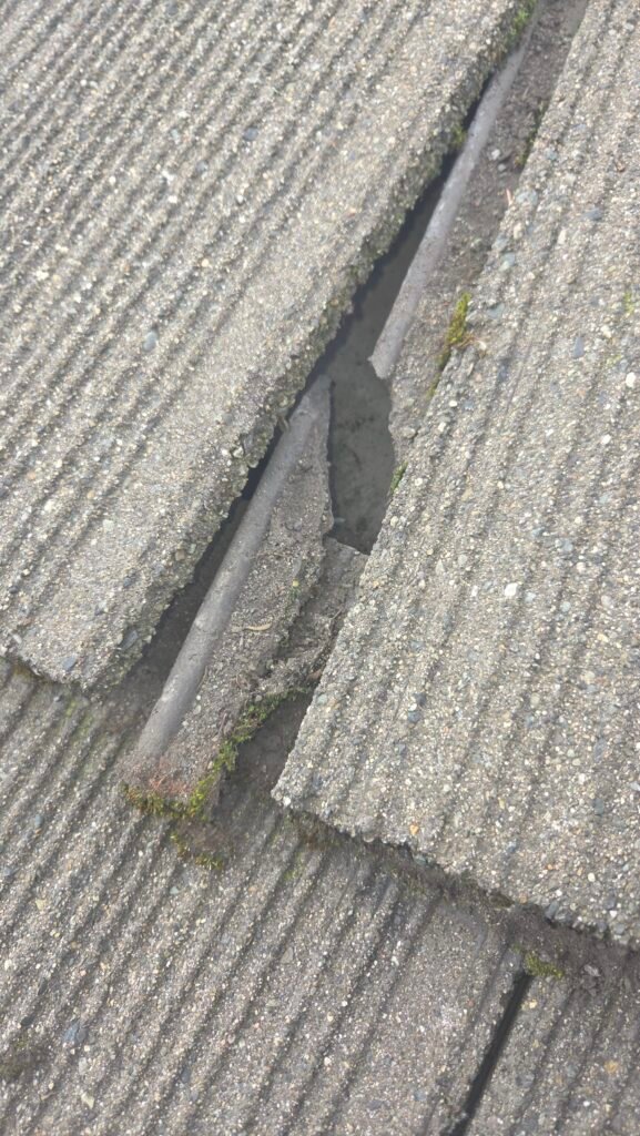 A broken bottom water channel on a concrete roof tile in Burnaby, with the broken channel piece sitting in place, where water escapes and leaks under the tiles.