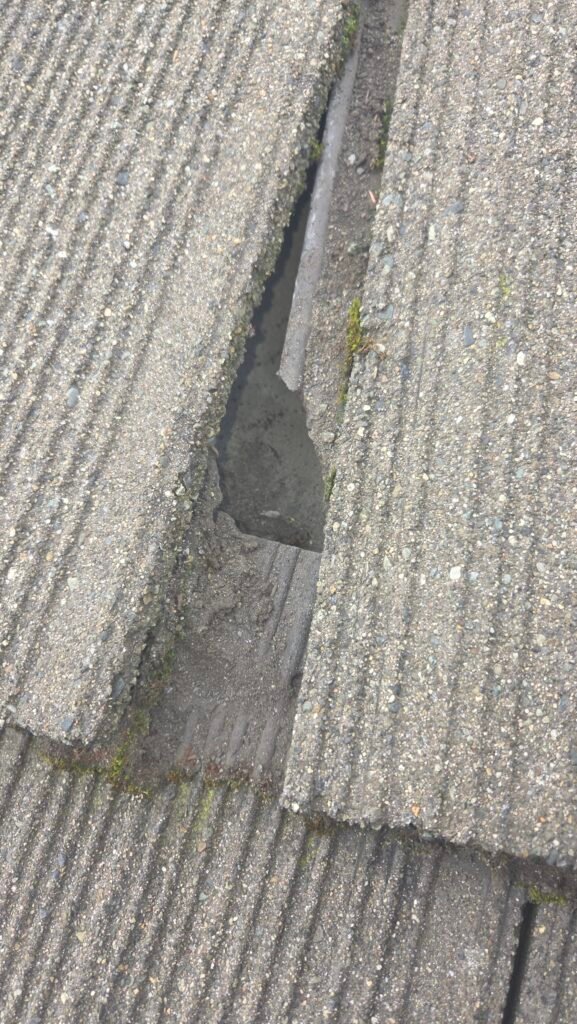 A lifted roof tile exposing a broken bottom water channel on the tile beneath, normally hidden by the overlap, in Burnaby.