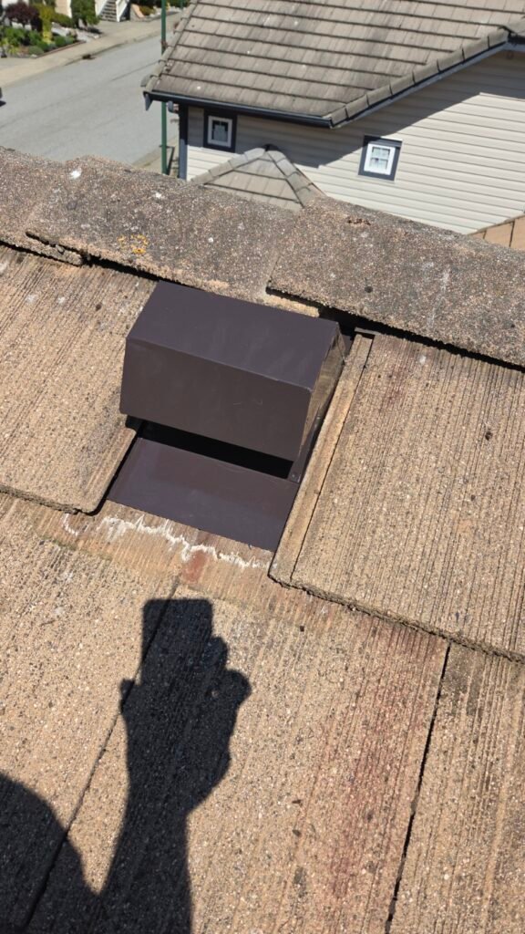 A finished painted metal hot welded gooseneck vent on a Coquitlam concrete tile roof with the tiles laid back down over the flange.