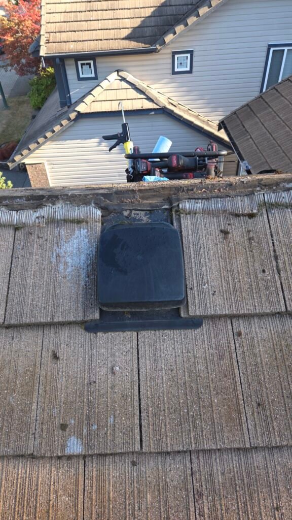 A plastic gooseneck roof vent on a Coquitlam concrete tile roof with its flange sealed to the field tiles with mastic, ridge tiles removed.
